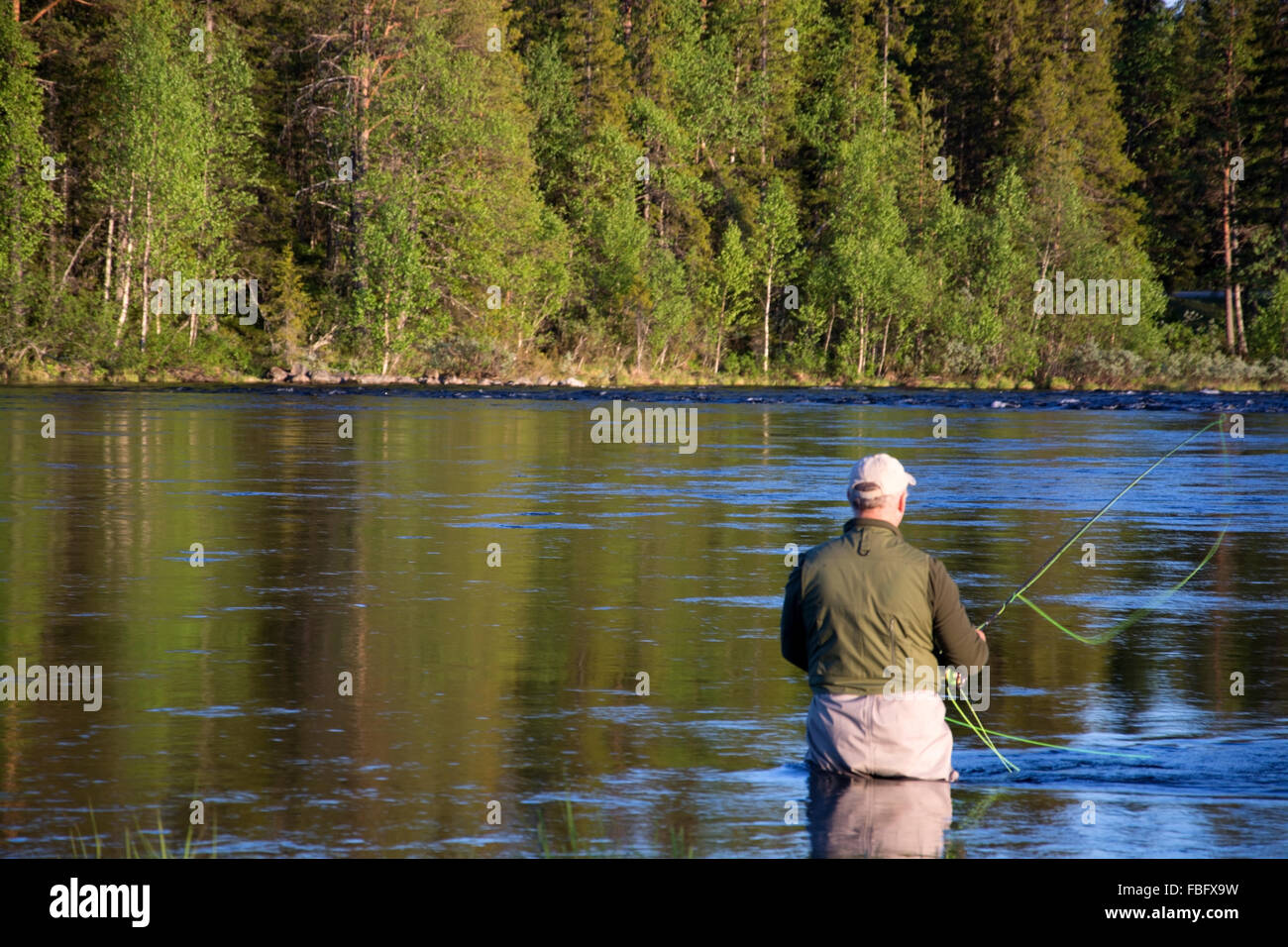 Il pescatore durante la pesca con la mosca in un fiume di sera. Foto Stock