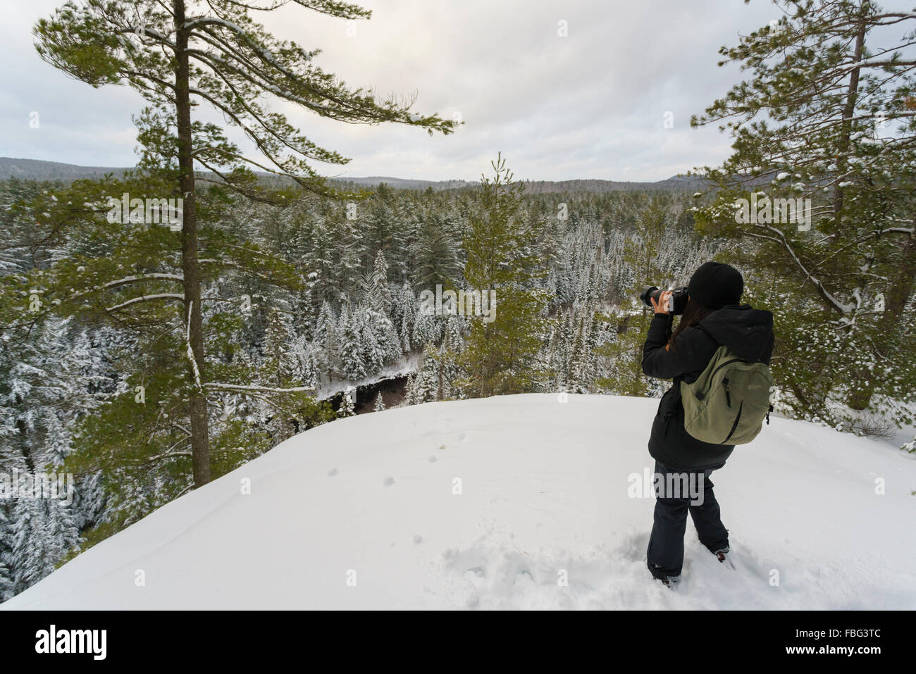 Giovane donna prende foto nella parte anteriore di una scogliera in inverno in Algonquin Provincial Park Foto Stock