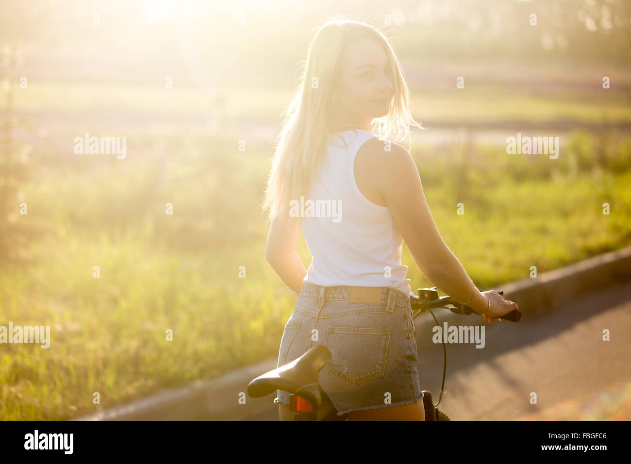 Ritratto di sportivo bella giovane donna a partire in bicicletta indossando casual serbatoio bianco top e jeans corti sulla strada in Brig Foto Stock