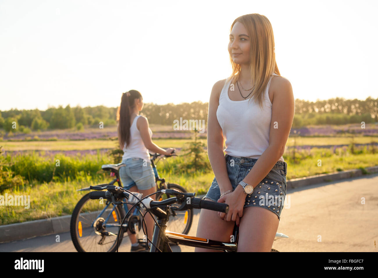 Bella ragazza bionda seduta su sport bike di indossare un abbigliamento informale sulla strada luminosa giornata estiva, cercando somewhe Foto Stock