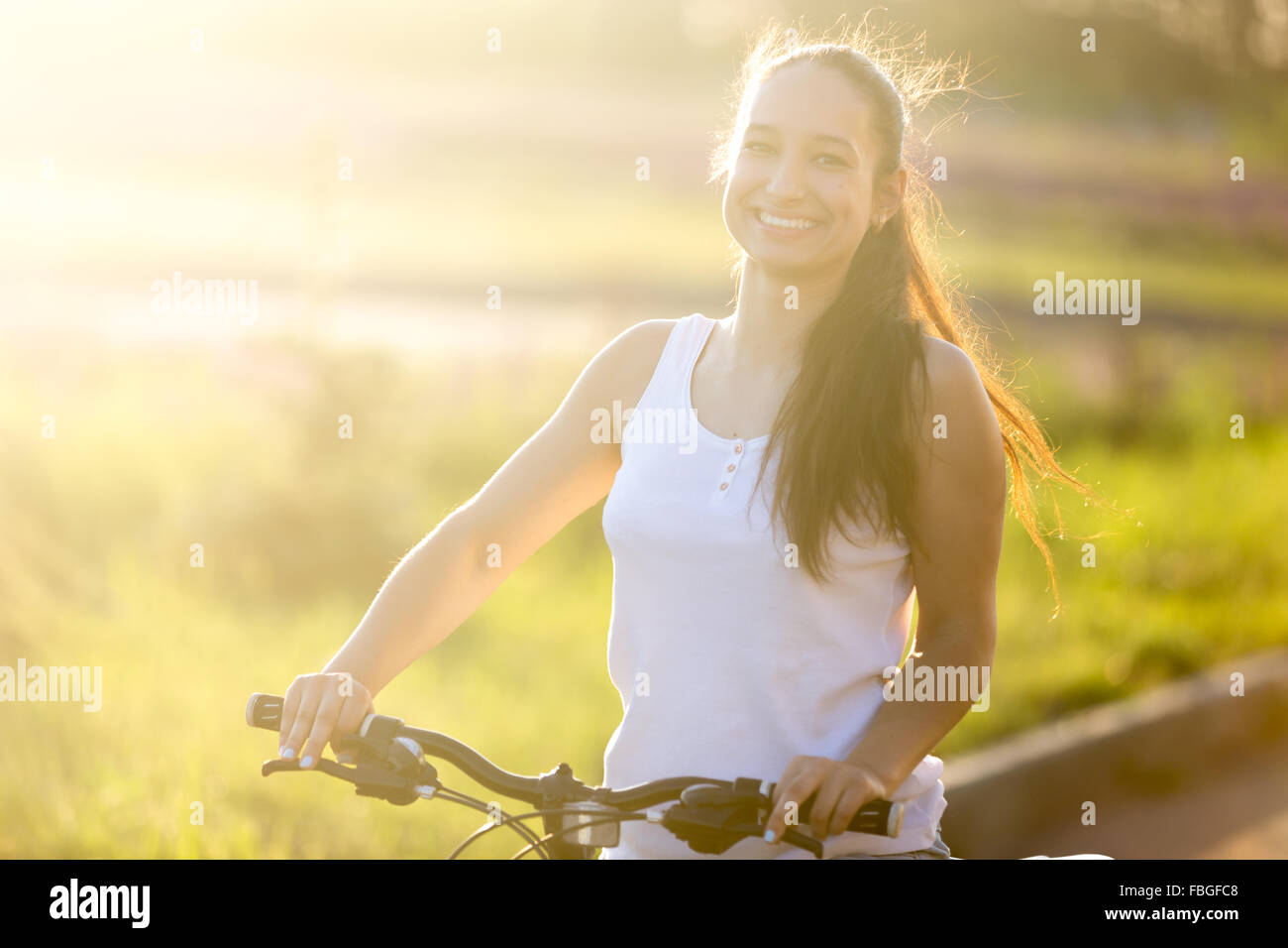 Ritratto di sorridenti giovani asiatici-caucasica donna posa sul moto di indossare abiti casual su strada in condizioni di luce solare intensa su Foto Stock
