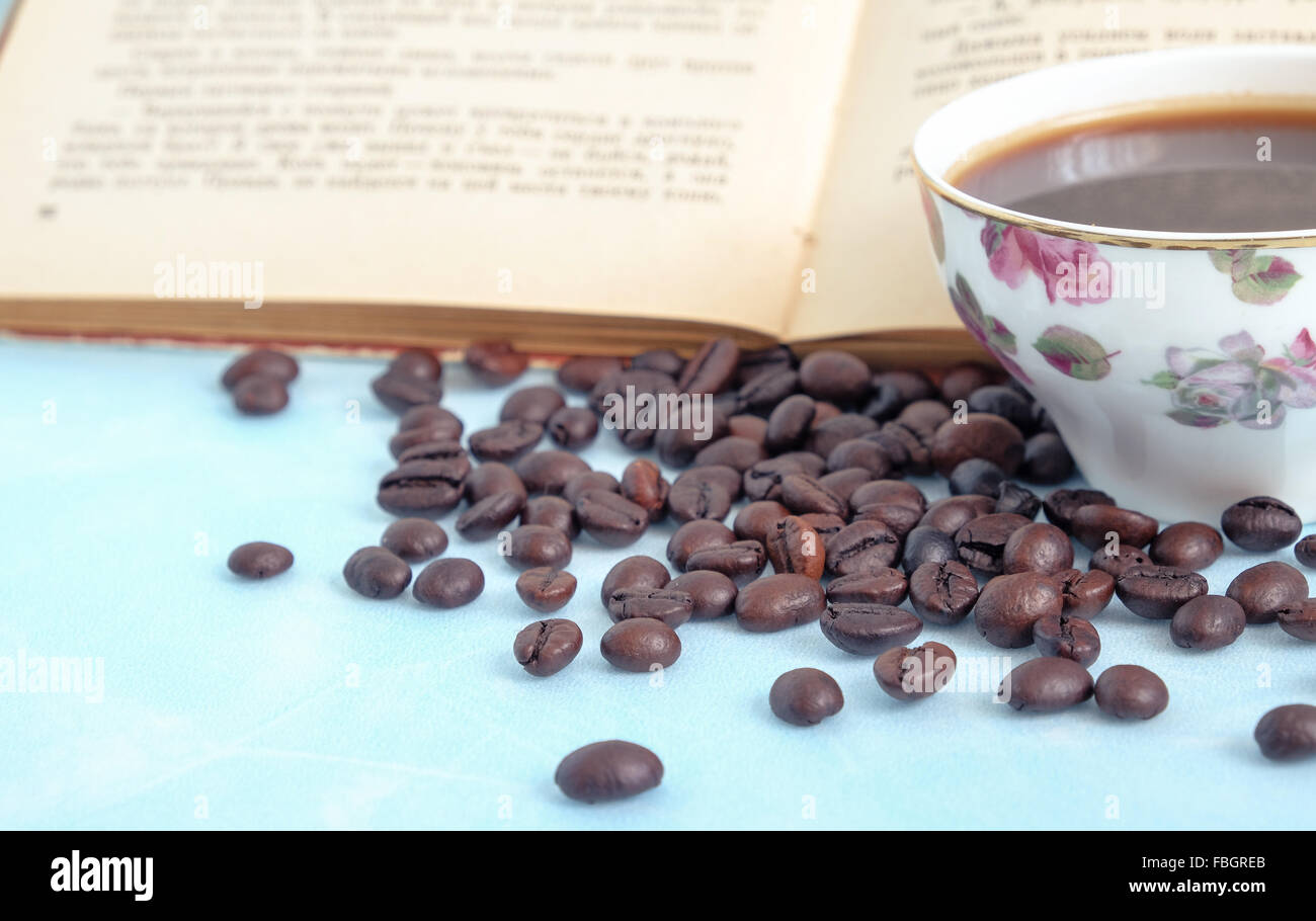 Chicchi di caffè tostati nello sfondo tazza di caffè caldo e libro aperto Foto Stock