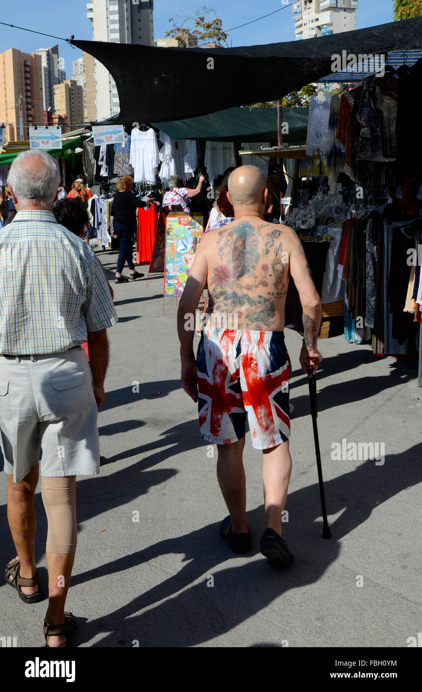 Turisti britannici che riporti il suo tatuato corpo superiore in shorts sono decorati con la Union Jack su un mercato settimanale a Benidorm, Alicante, Foto Stock
