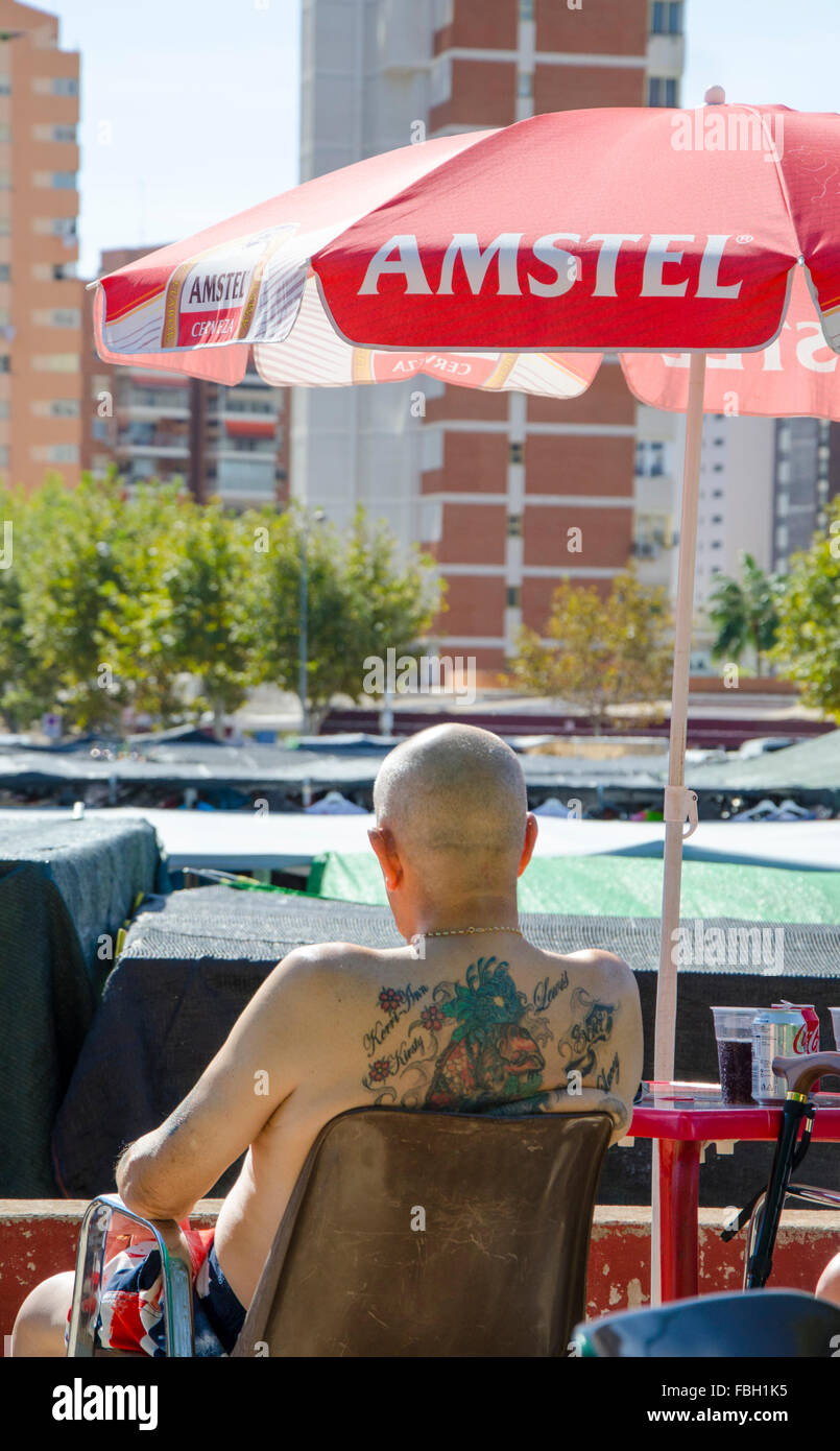 Turisti britannici che riporti il suo tatuato corpo superiore in shorts sono decorati con la Union Jack pub sulla terazza in un mercato settimanale Benid Foto Stock