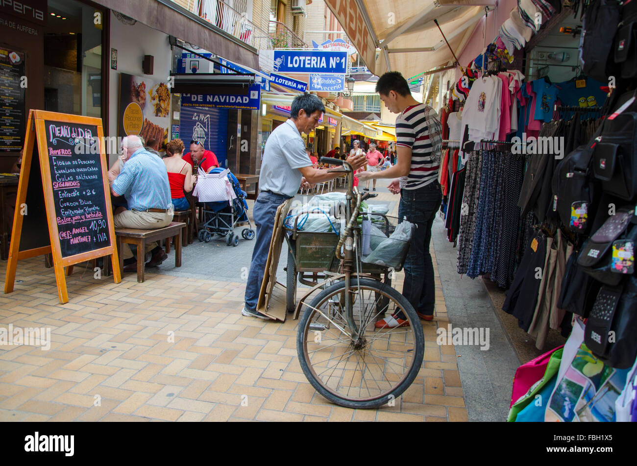 Uomo asiatico vende le verdure dalla sua bicicletta ad un altro asiatici in zona pedonale di Benidorm, Alicante, Spagna Foto Stock