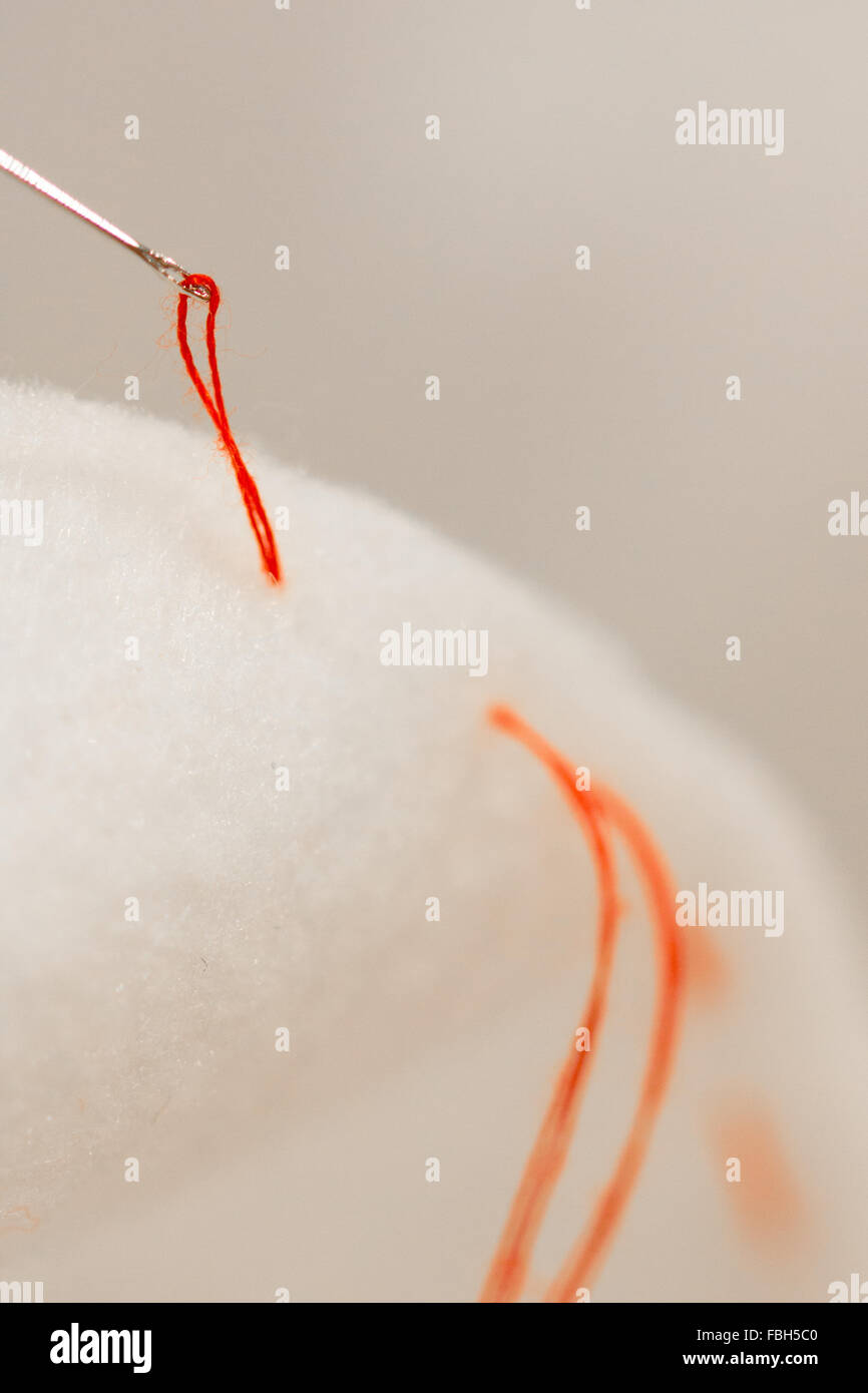 Un ago cucito insieme i due pezzi di tessuto bianco con un filo rosso. Foto Stock