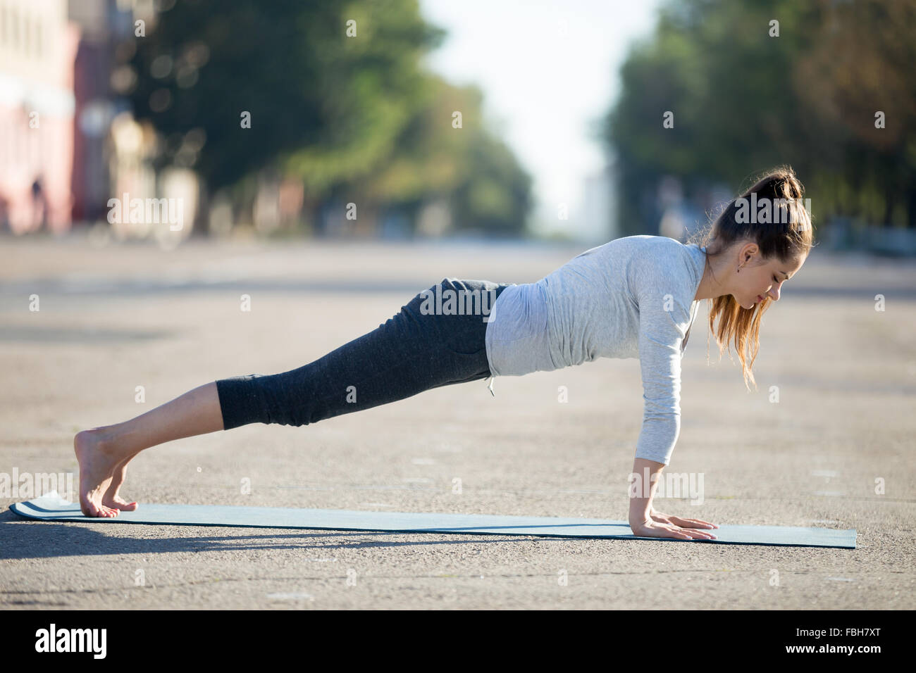 Lo Yoga nella città: bella giovane sportivo da donna che indossa abbigliamento sportivo che lavora fuori sulla strada a giornata estiva, facendo plank postura, Foto Stock