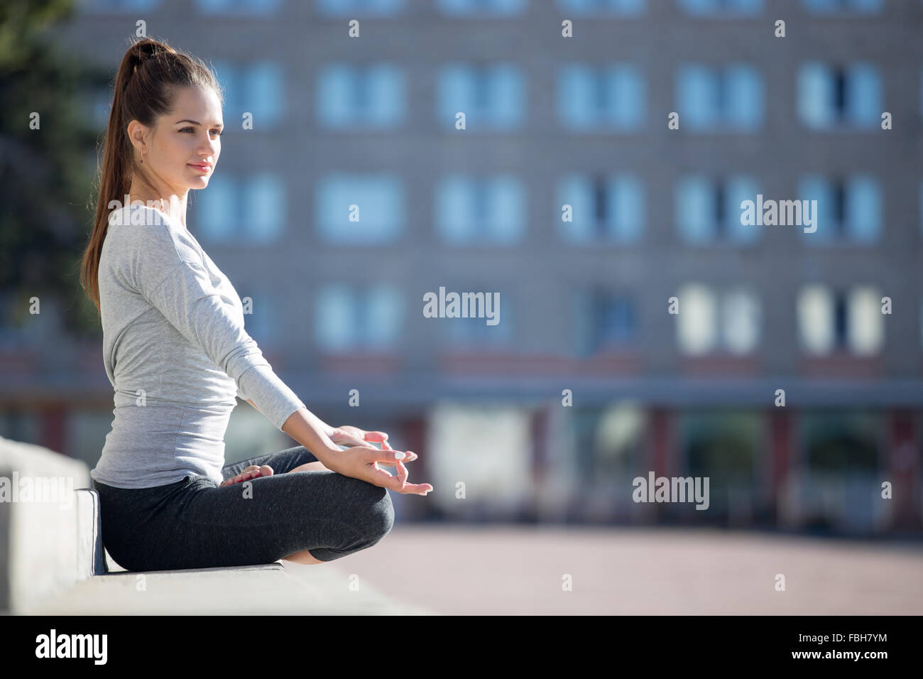 Lo Yoga nella città: bellissima giovane donna fit meditando, respirazione, seduto in Loto la postura di fronte all edificio sulla str Foto Stock