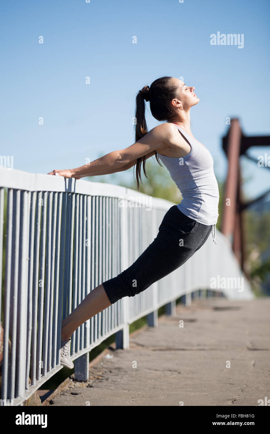 Lo Yoga nella città: bella giovane montare la donna che lavora fuori sul vecchio ponte sul giorno di estate, facendo stretching, il riscaldamento degli esercizi Foto Stock