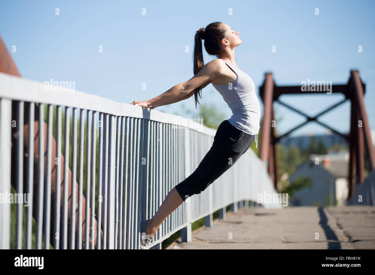 Lo Yoga nella città: sportivo bella ragazza adolescente che lavora fuori sul vecchio ponte sul giorno di estate, facendo backbend sulla ringhiera del riscaldamento, Foto Stock