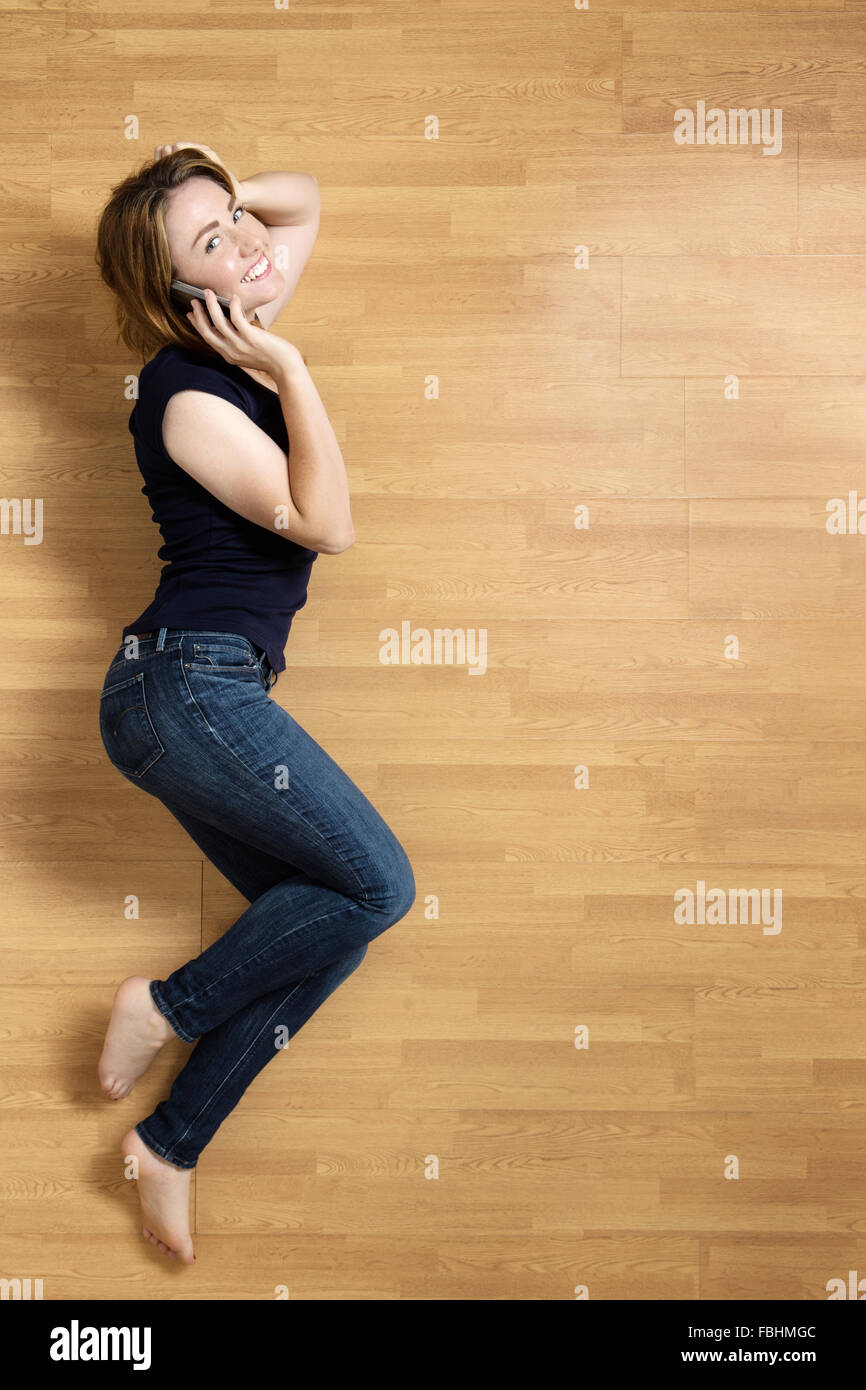 Donna sorridente giacente sul suo lato sinistro sul pavimento, appoggiata sul suo gomito, con il suo cellulare al suo orecchio destro. Foto Stock