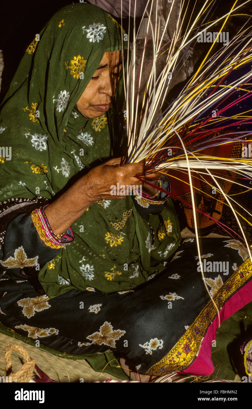 Qurum, Oman. Donna di mezza età lavora con paglia per rendere un cestello. Festival di Muscat, dimostrando artigianato tradizionale. Foto Stock