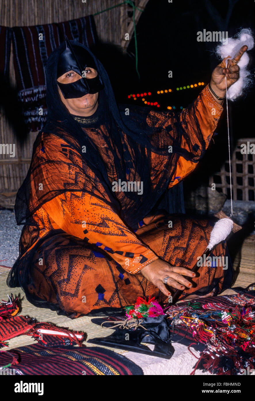 Qurum, Oman. Di mezza età donna mascherata di filatura da filo di lana. Il Muscat Festival, dimostrando Omani tradizionale artigianato. Foto Stock
