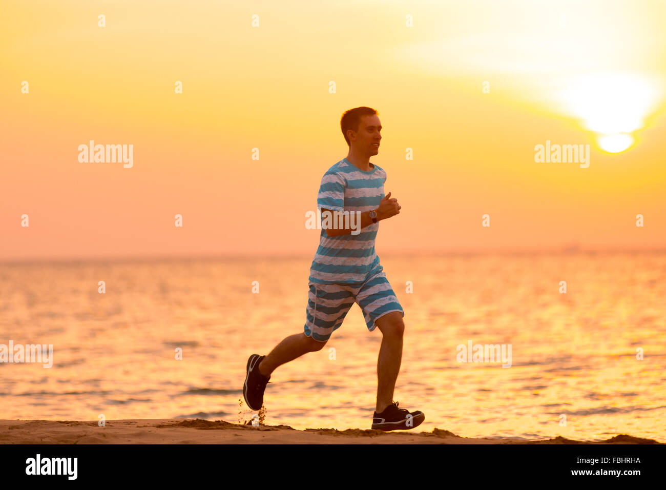 Uno stile di vita sano: bel giovane uomo che lavora fuori all'aperto, corre veloce sulla sabbia a riva al tramonto o l'alba Foto Stock