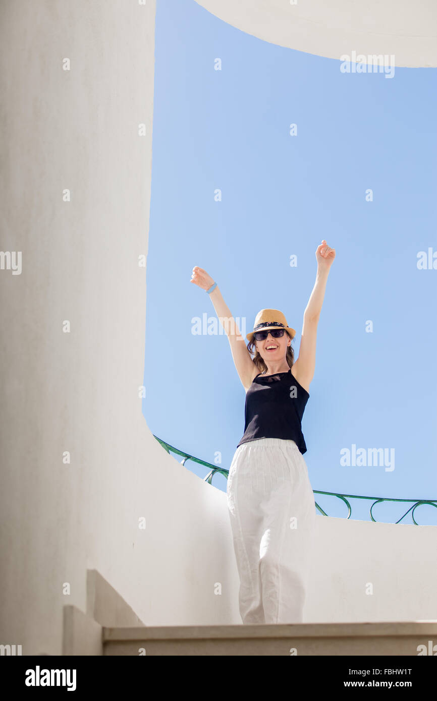 Giovane bella donna nel cappello e mantello di lino balli presso la terrazza estiva soleggiata con pareti in stucco in città bianca, divertendosi, feelin Foto Stock