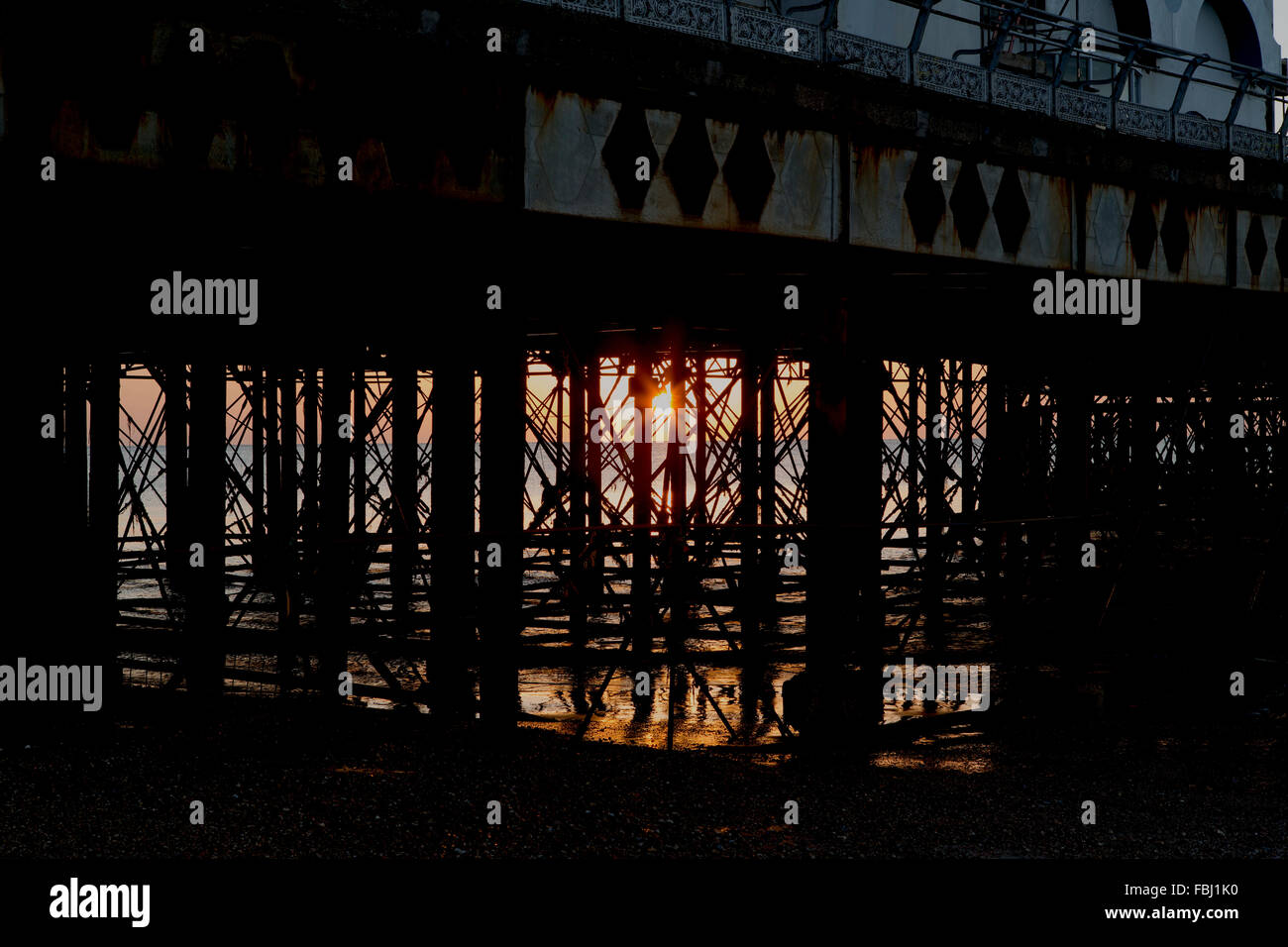 Sunrise dietro South Parade pier a Southsea. Sunburst risplende attraverso la formazione di ruggine pontili. Bagliore dorato con riflessione nel mare. Foto Stock