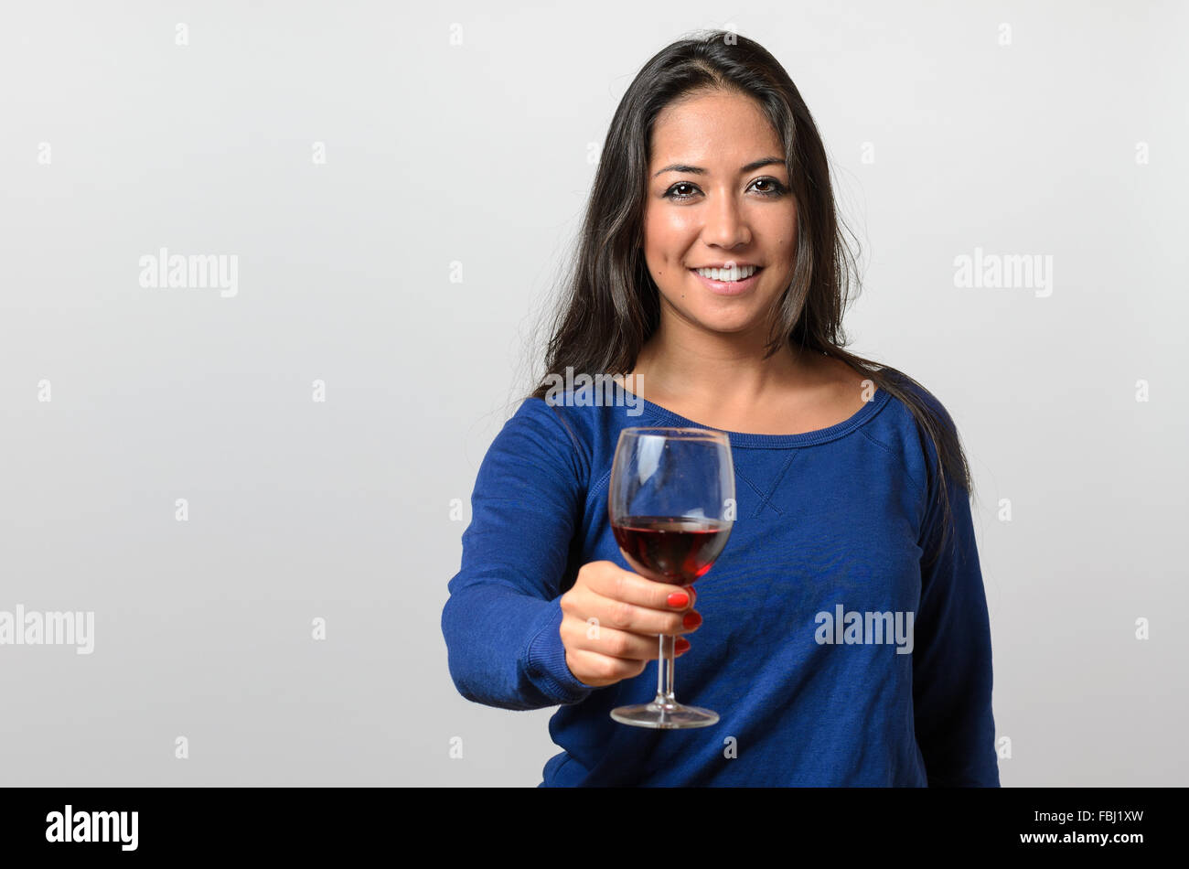 Felice attraente giovane donna la tostatura con un bicchiere di vino rosso sollevandola per la fotocamera come la celebra un occasione speciale Foto Stock