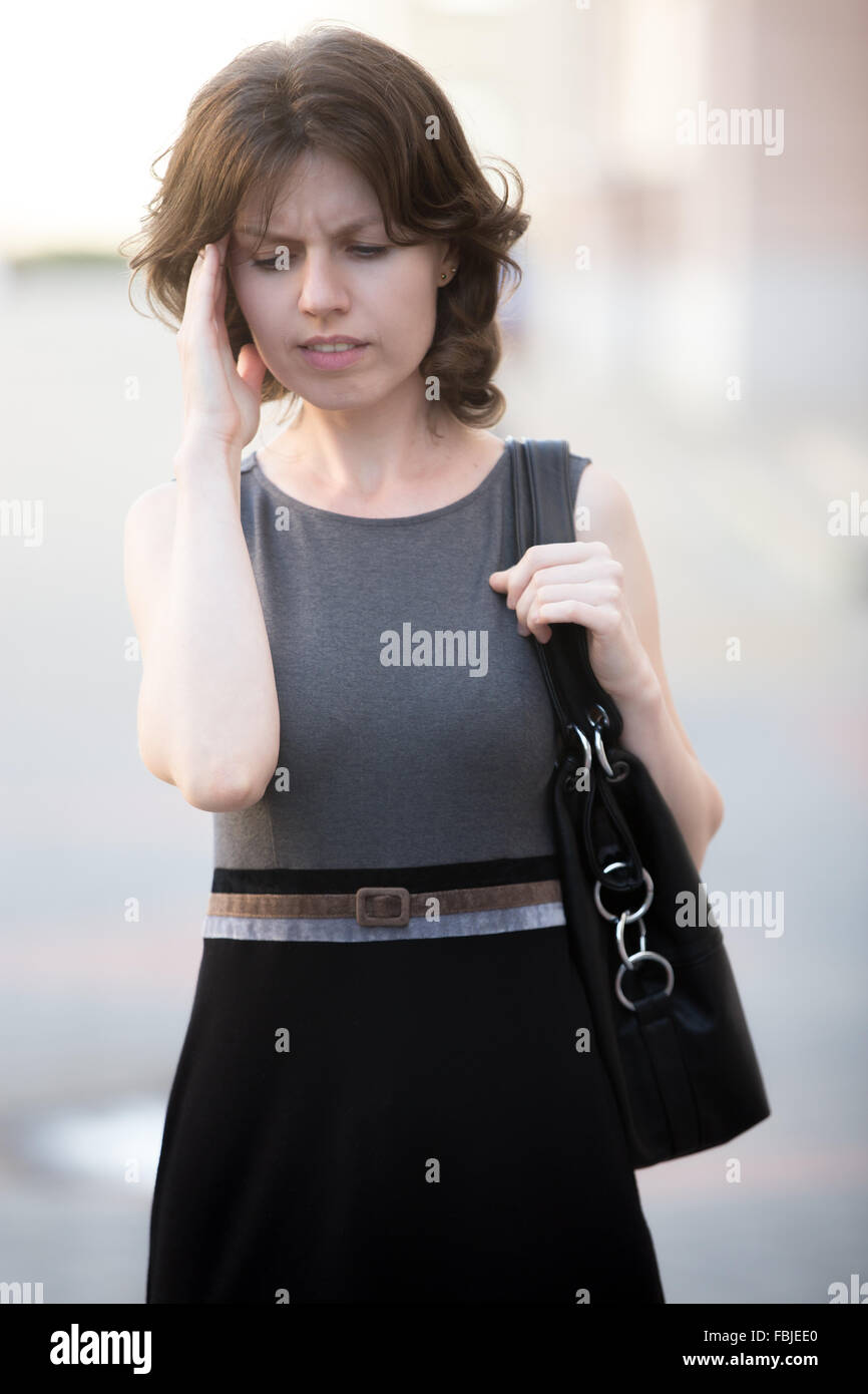 Ritratto di giovane donna ufficio camminando sulla strada in estate, accigliata, sensazione di stanchezza o confuso, tenendo la testa con la mano Foto Stock