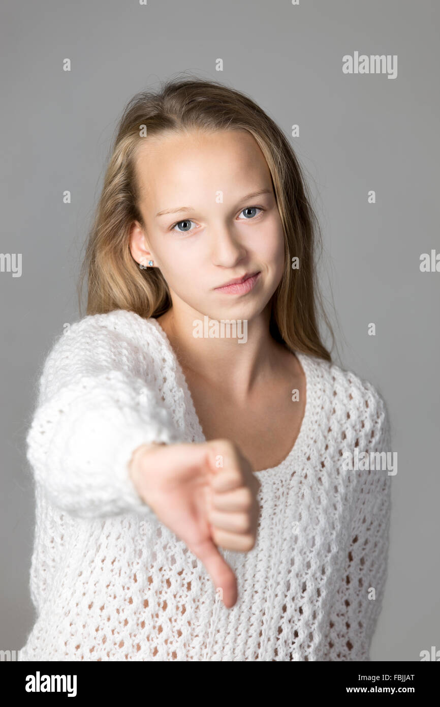 Ritratto di infelice casual bella ragazza caucasica indossando bianco felpa lavorata a maglia, che mostra il pollice verso il basso guardando la fotocamera Foto Stock