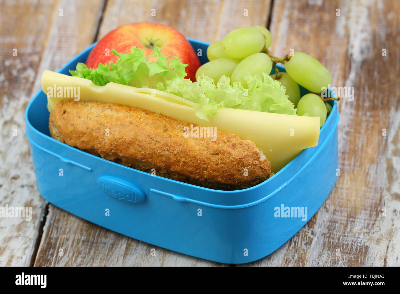 Pranzo sano scatola contenente marrone Rotolo di pane con formaggio e lattuga, Rosso mela e uva Foto Stock