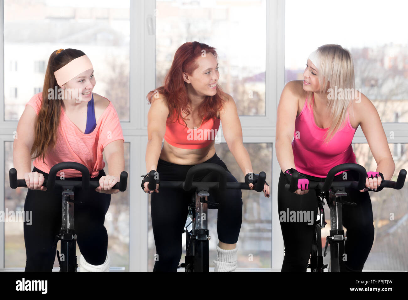 La pratica di fitness, gruppo di montare tre belle femmine allegro in bicicletta nel club sportivo, facendo esercizi cardio per dimagrire Foto Stock