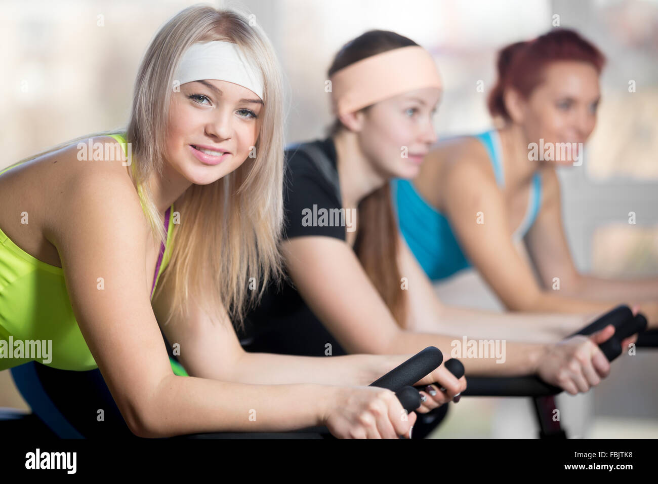 La pratica di fitness, gruppo di montare tre belle femmine allegro in bicicletta nel club sportivo, facendo esercizi cardio per dimagrire Foto Stock