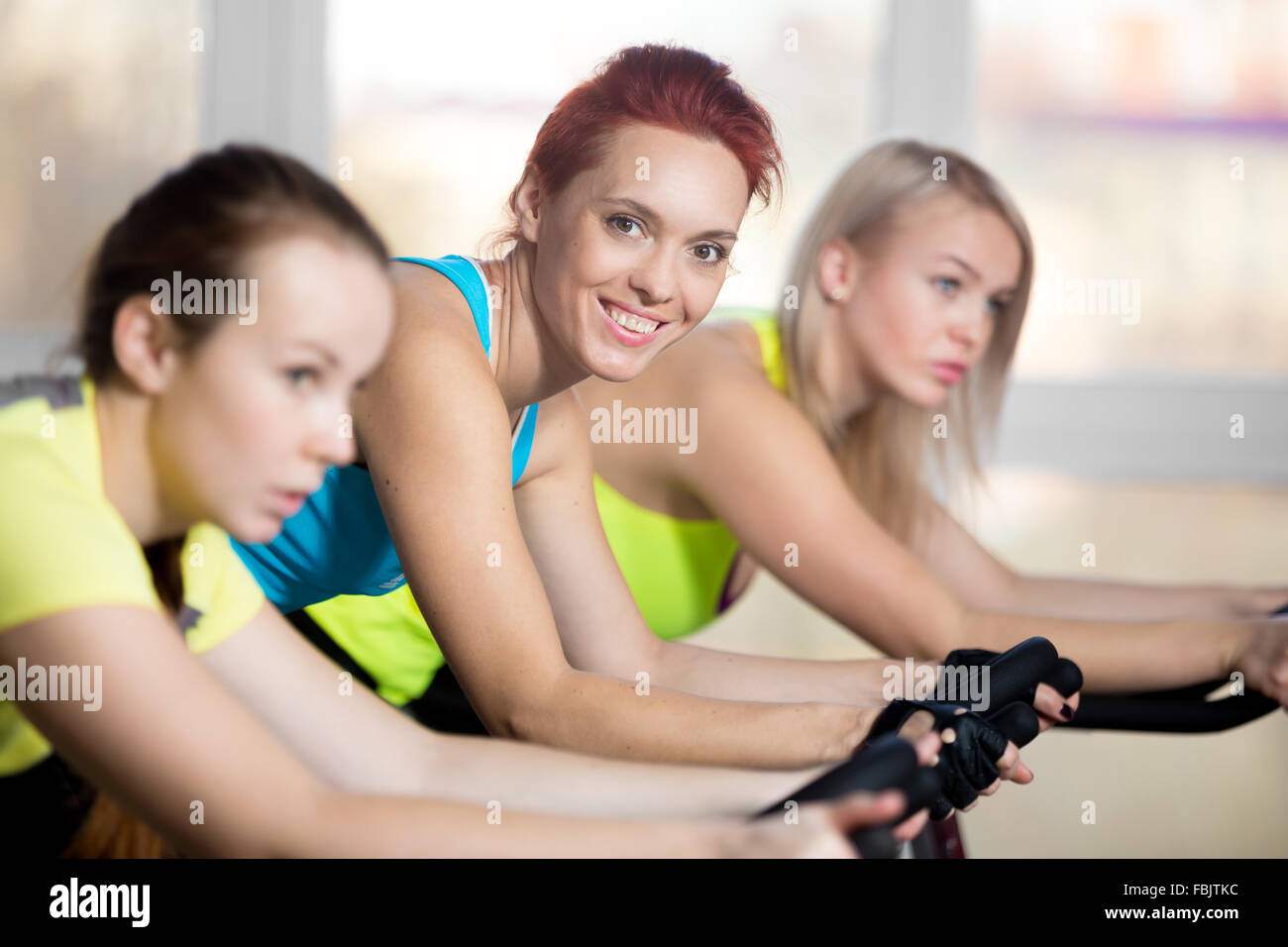 Ritratto di bella allegro friendly sorridente giovane donna in blu in alto del serbatoio esercitando sul ciclo in sports club con il gruppo Foto Stock