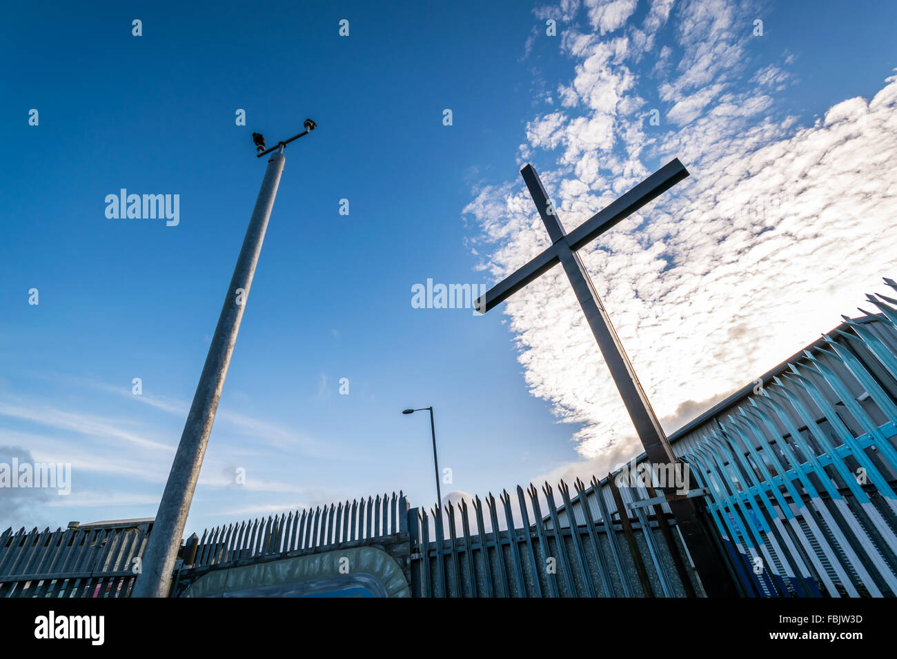 Segno dei tempi, un religioso croce sta al fianco di sistema di sicurezza con telecamere a Belfast linea di pace Foto Stock