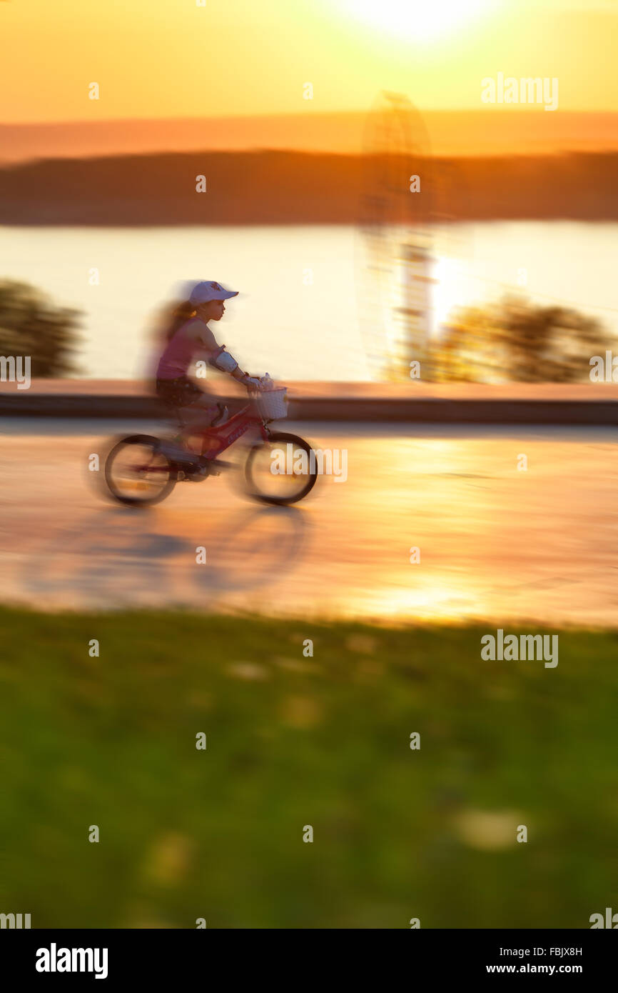 Bambino una corsa in bicicletta lungo il fiume di sera Foto Stock