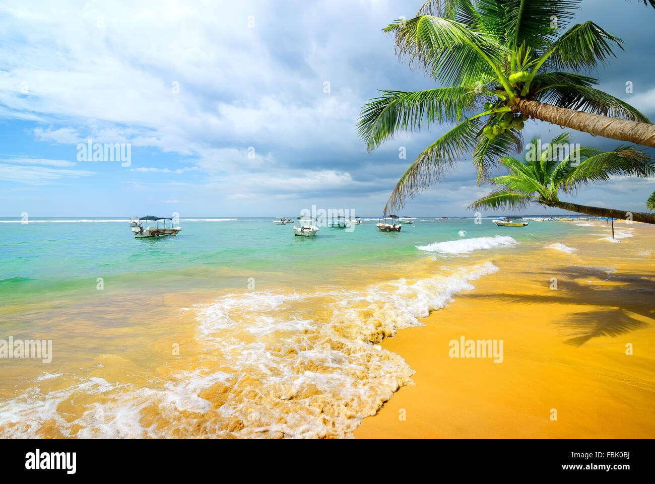 Barche in oceano vicino spiaggia di sabbia e palme Foto Stock