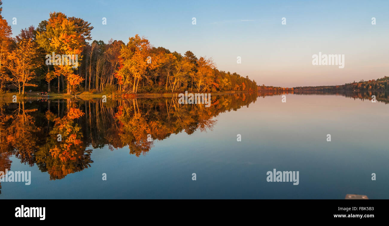 Specchio-simili riflessioni e bagliore arancione sulla foresta a nord del lago Ontario al tramonto su una tarda estate del giorno Foto Stock
