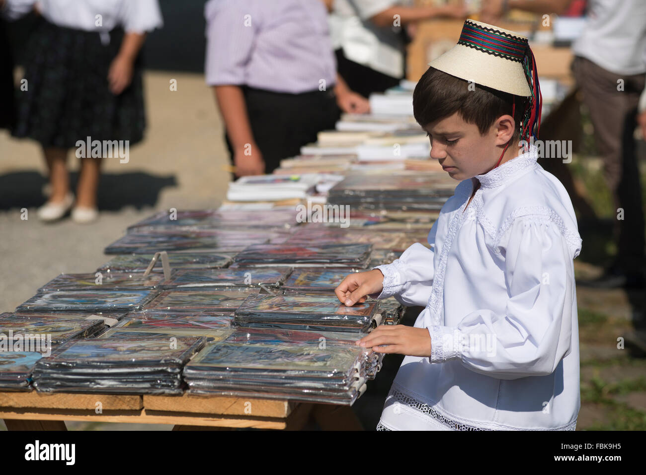 Ragazzo in costume tradizionale vende oggetti religiosi esterni nel distretto di Maramures, Romania Foto Stock