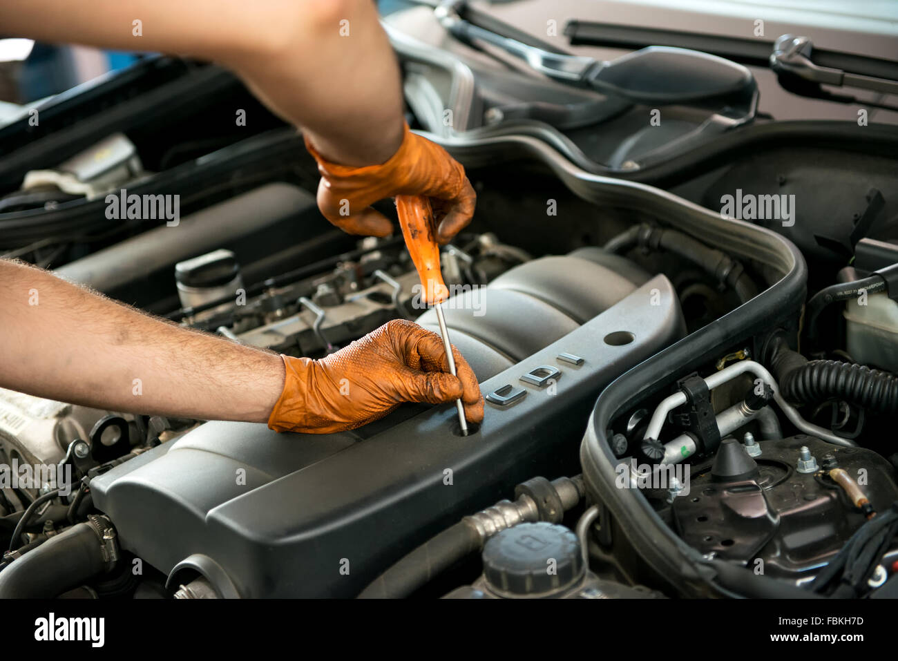 In prossimità delle mani con guanti di un maschio meccanico che lavora su una vettura a motore con un cacciavite in un workshop durante un servizio Foto Stock