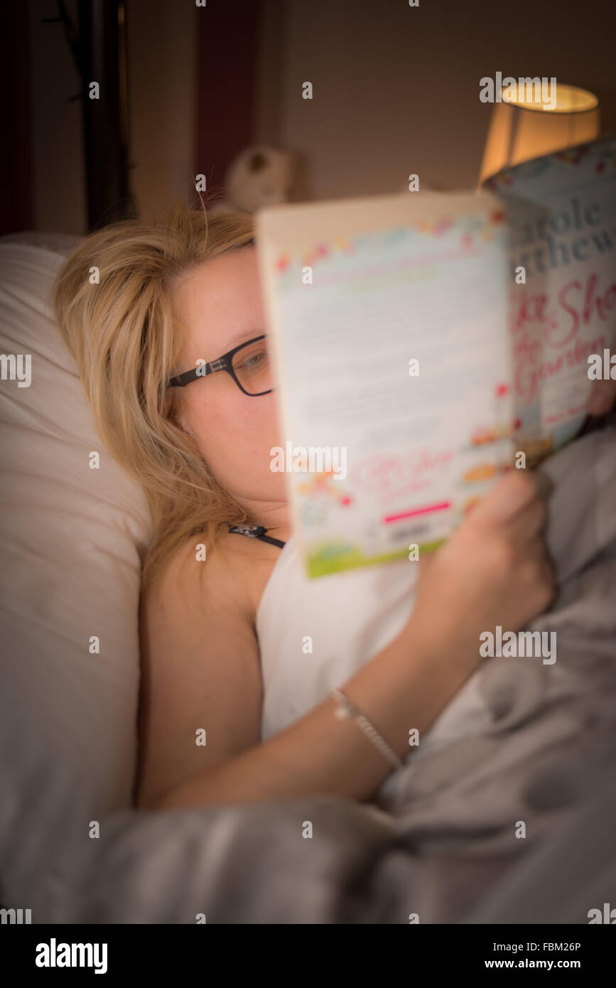 Una donna che legge un libro a letto Foto Stock