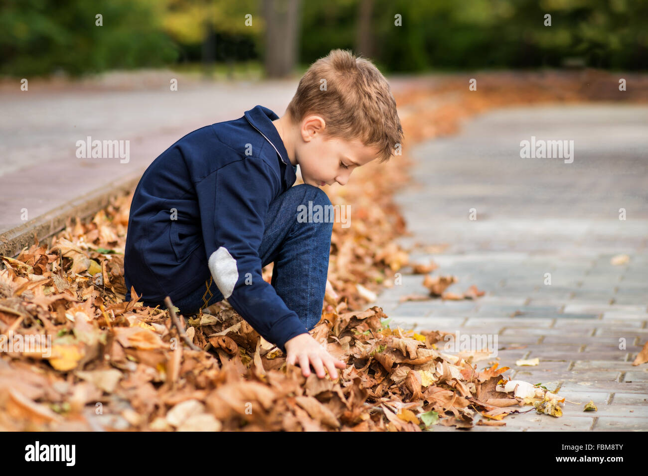 Ragazzo seduto in strada tra foglie di autunno Foto Stock