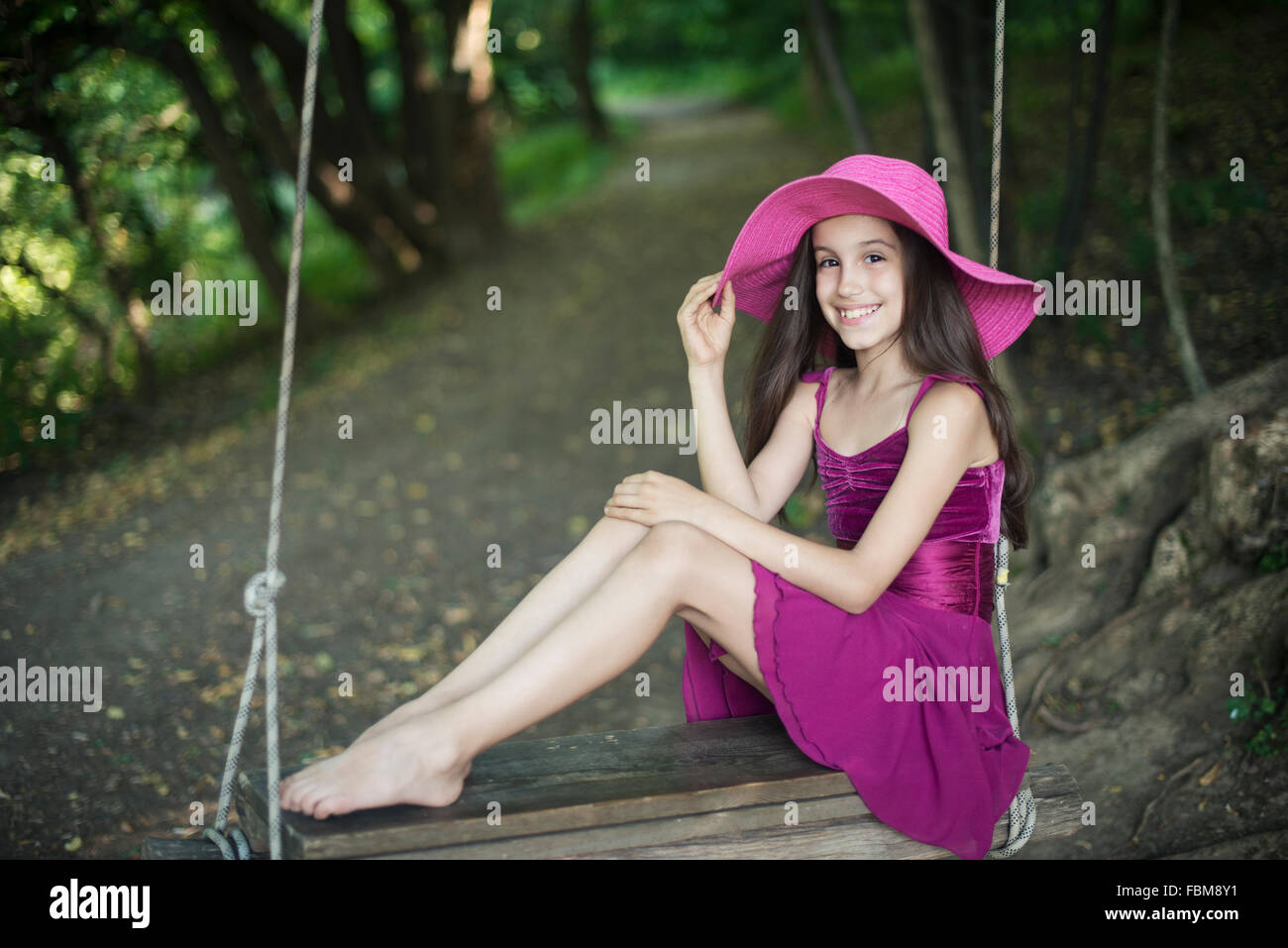 Ragazza in rosa seduto su una corda swing in una foresta Foto Stock