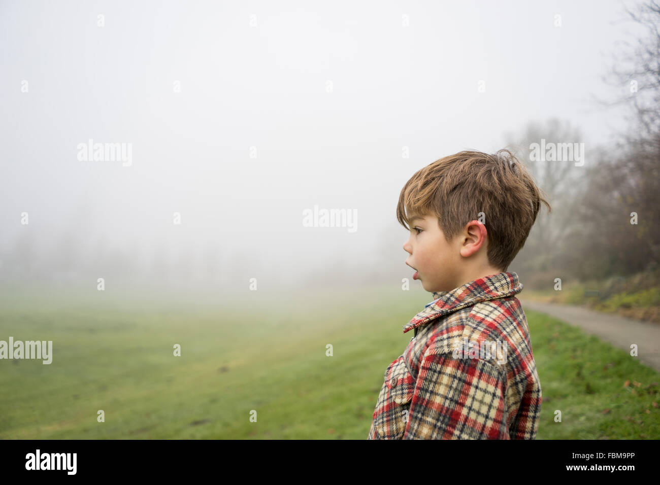 Profilo laterale di un ragazzo che sta in un parco su nebbioso giorno Foto Stock