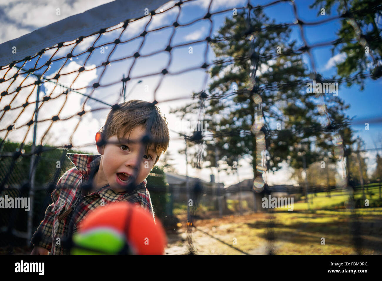 Vista attraverso una rete di un ragazzino gettando palla da tennis Foto Stock