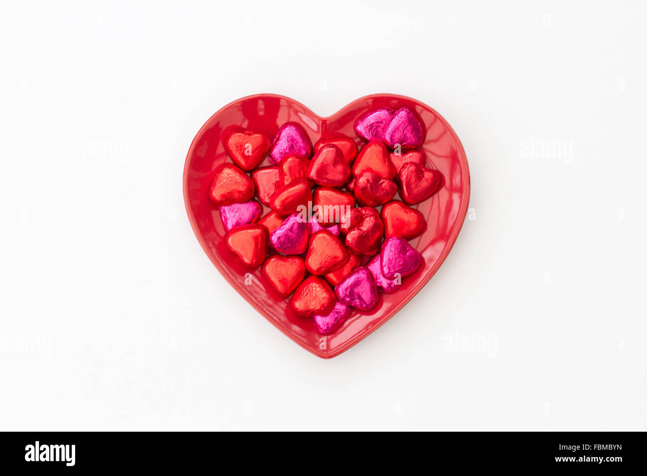 Un rosso a forma di cuore il giorno di san valentino piatto pieno di cioccolatini isolato su un fondo bianco. Foto Stock