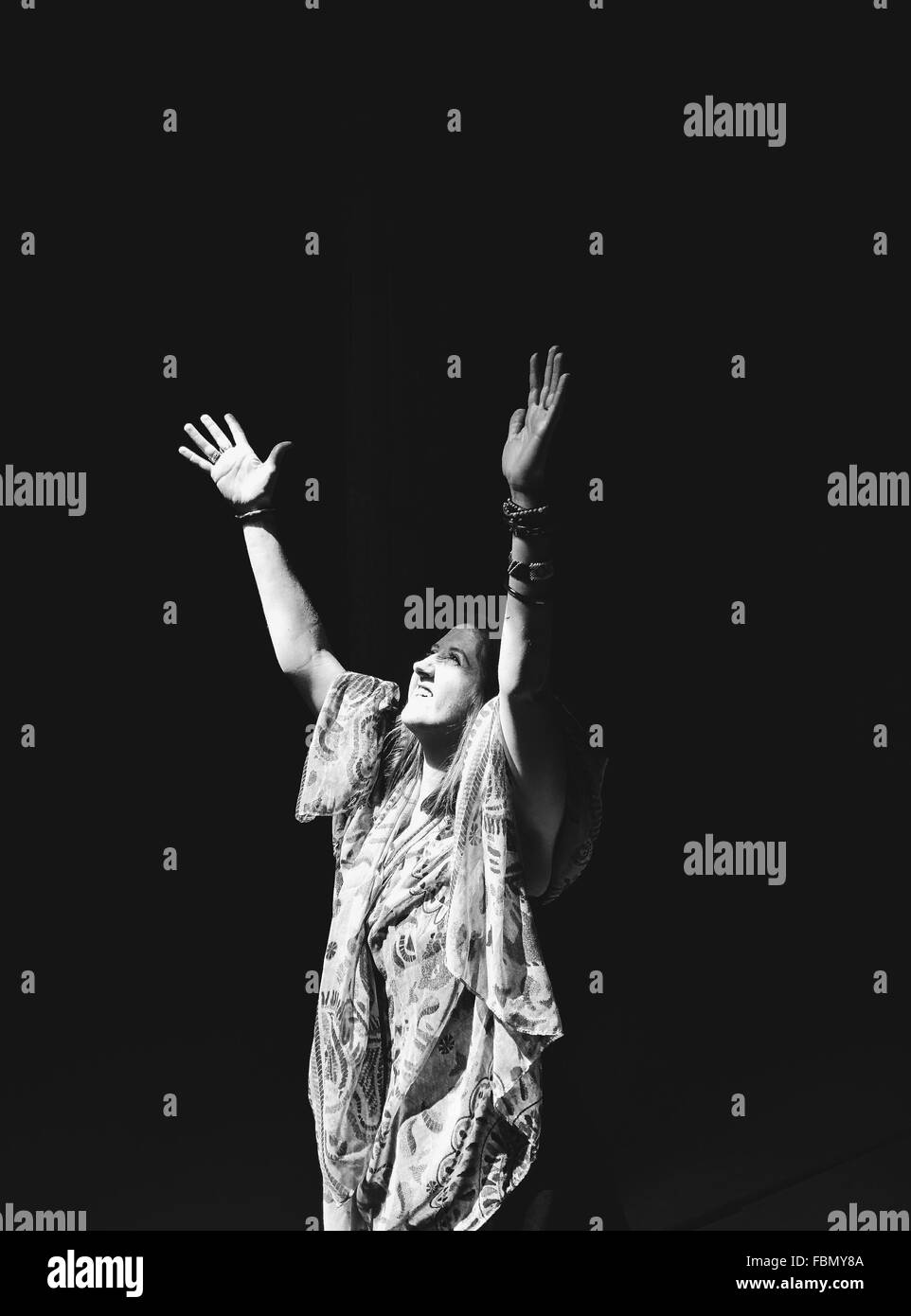 Giovane donna alzando le mani su sfondo nero Foto Stock