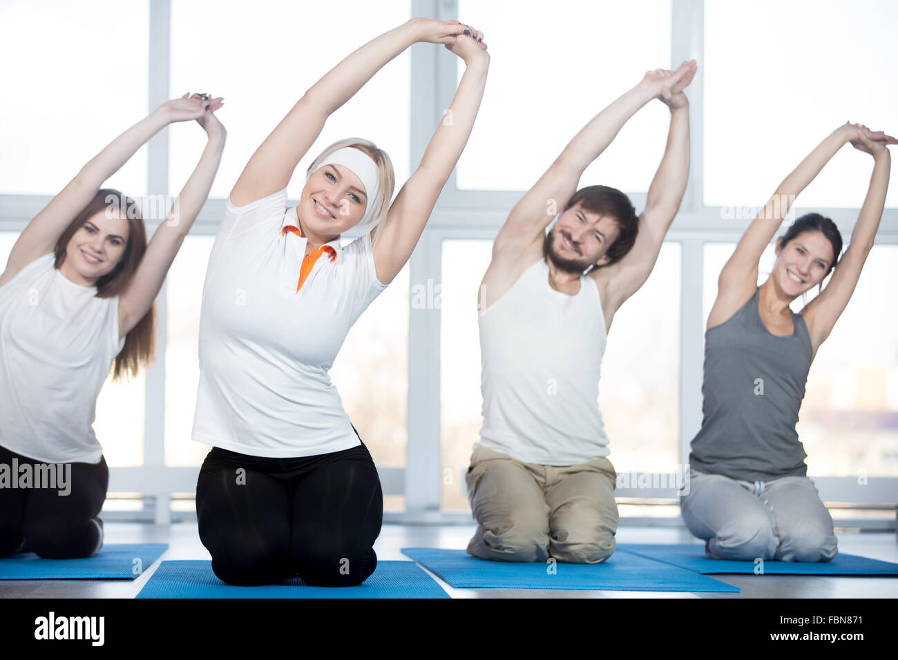 Fitness, stretching pratica, gruppo di quattro bellissimi felice montare i giovani a lavorare nel club sportivo, facendo piegare laterale Foto Stock