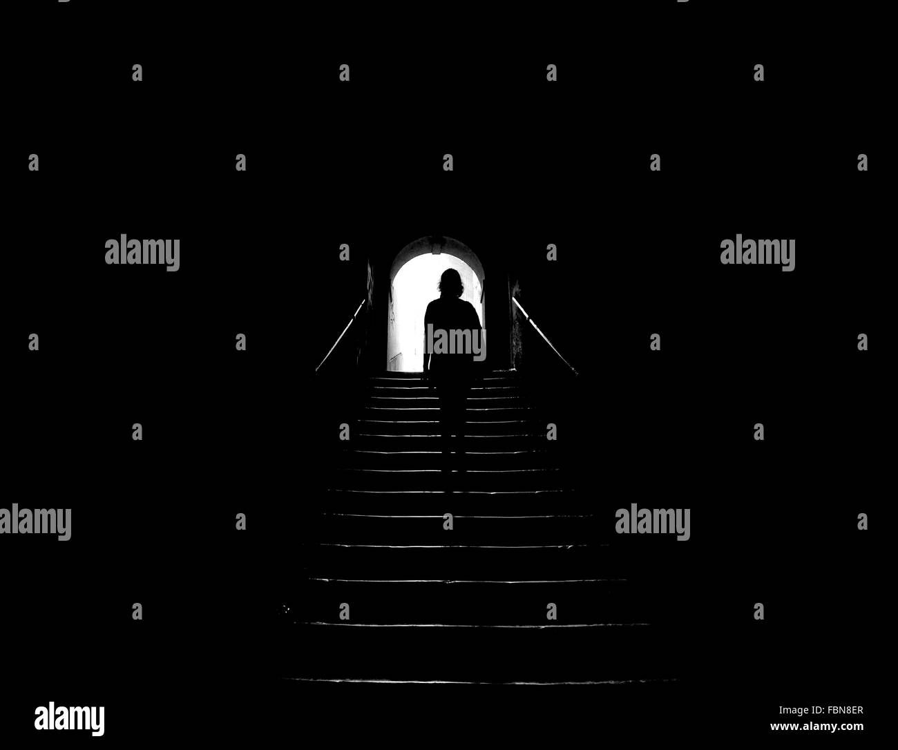 Vista posteriore di Silhouette donna su scala nel buio del tunnel Foto Stock
