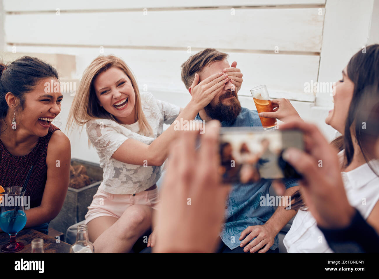 Gruppo di amici divertendosi ad una festa con l uomo di scattare una foto su un telefono intelligente. Giovani godendo di una festa insieme. Foto Stock