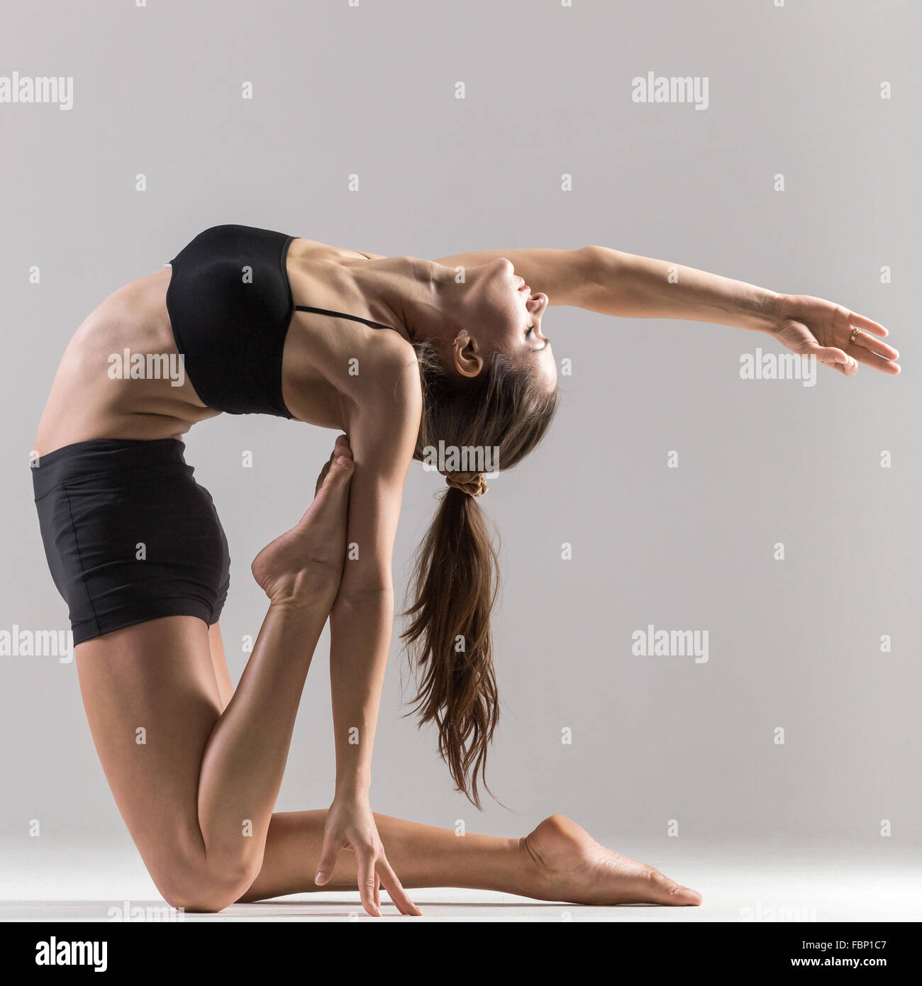 Bella sportiva ragazza Yogi pratiche yoga asana, Ustrasana, Ushtrasana, Camel pongono su uno sfondo grigio, chiave di basso shot Foto Stock