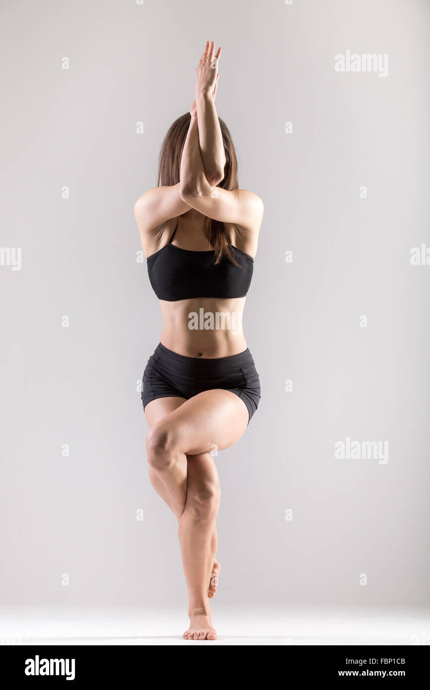 Bella sportiva ragazza Yogi pratiche yoga asana, Garudasana,la posizione dell'Aquila su sfondo grigio, chiave di basso shot Foto Stock