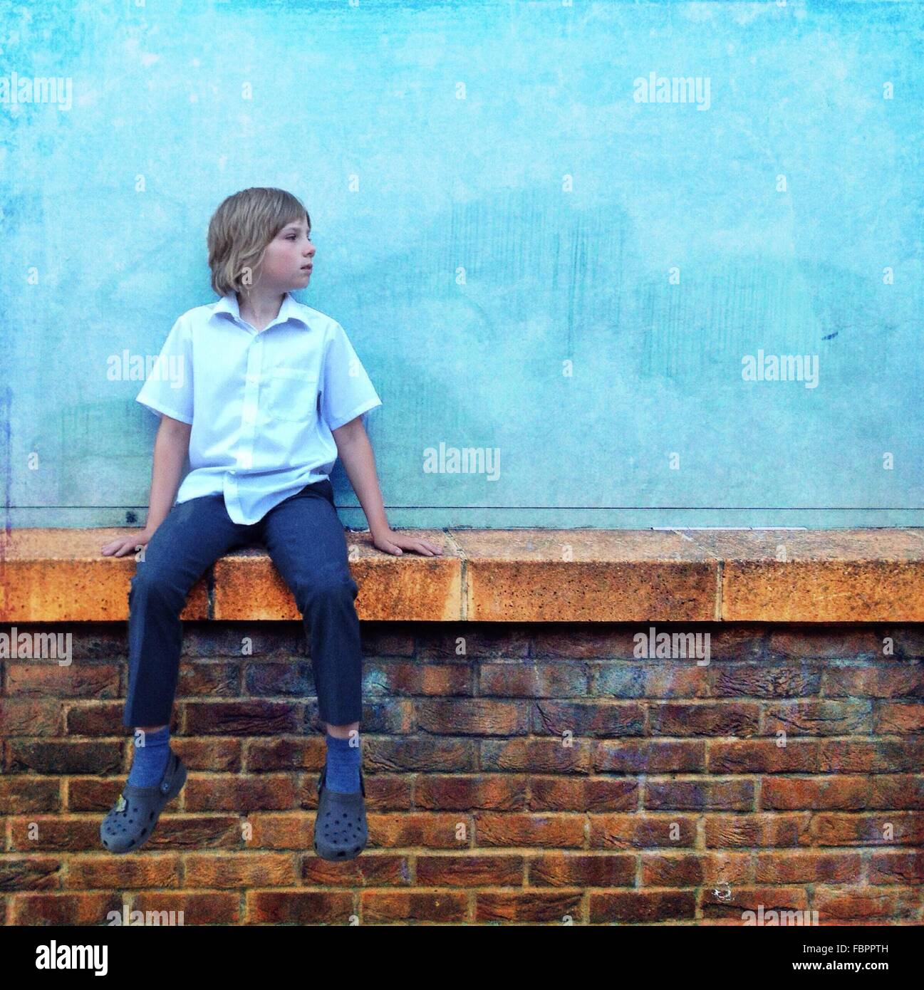 Ragazzo adolescente indossando Maglietta Blu e Jeans seduti sulla parete Foto Stock