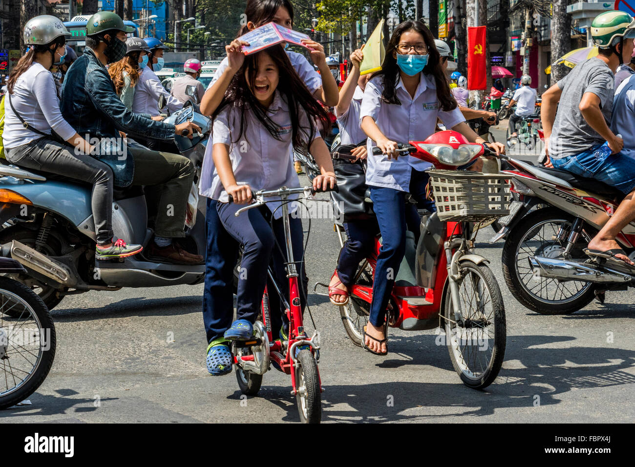 Le fanciulle felici uno con maschera per proteggere la sua da inquinamento cicli di equitazione con pillion passeggeri in Ho Chi Minh city Vietnam Foto Stock