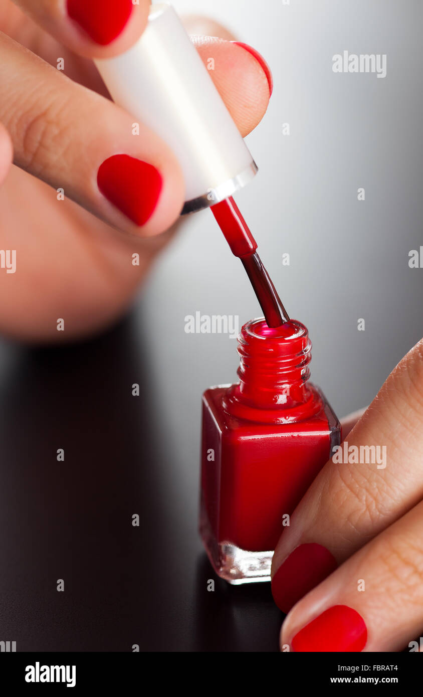Aprire la bottiglia di rosso di smalto per unghie in donna curati palms su sfondo nero. Foto Stock