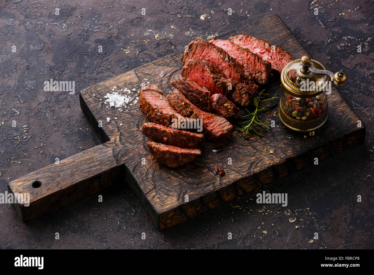 Fette di mezzo raro grigliate di carne di manzo e pepe mulino sul tagliere di legno Foto Stock