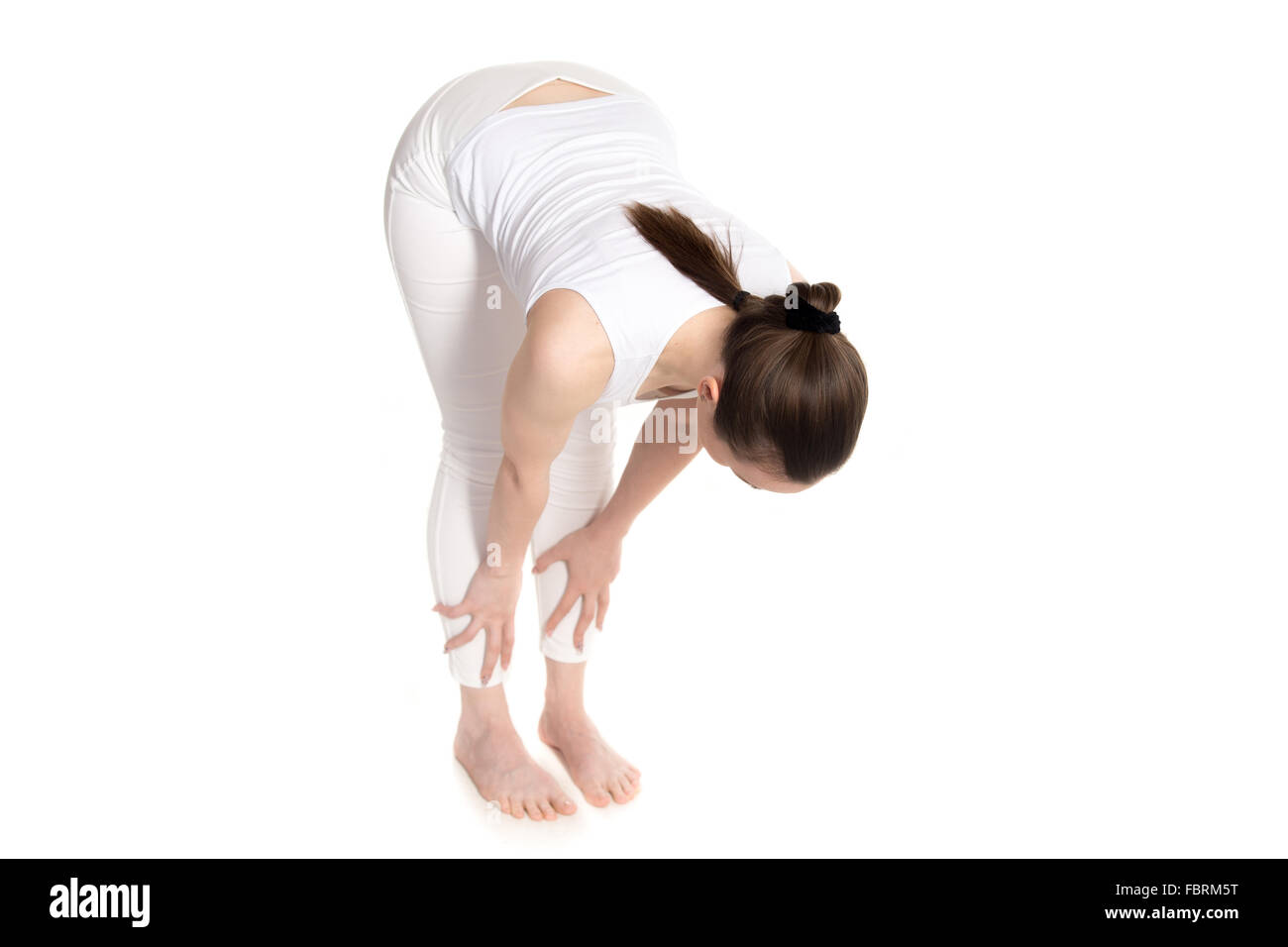 Sporty bella giovane donna in bianco sportswear facendo mezza flessione in avanti esercizio per la flessibilità della colonna vertebrale, Uttanasana pongono facile Foto Stock